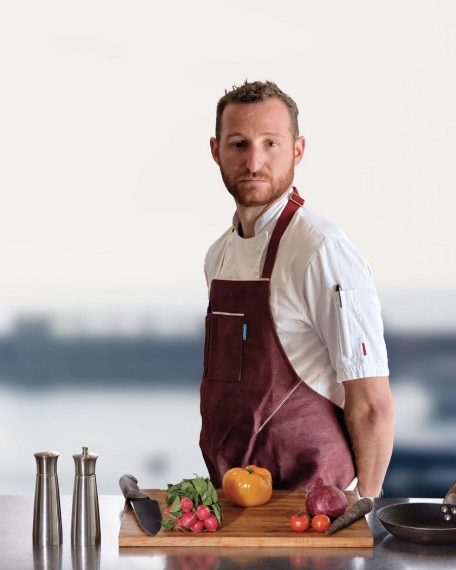 Ivan Holmes, private chef, in whites and apron at his kitchen bench